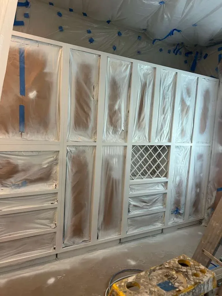 Kitchen cabinet boxes fully masked and freshly spray painted during cabinet refinishing in Fulshear, Texas.