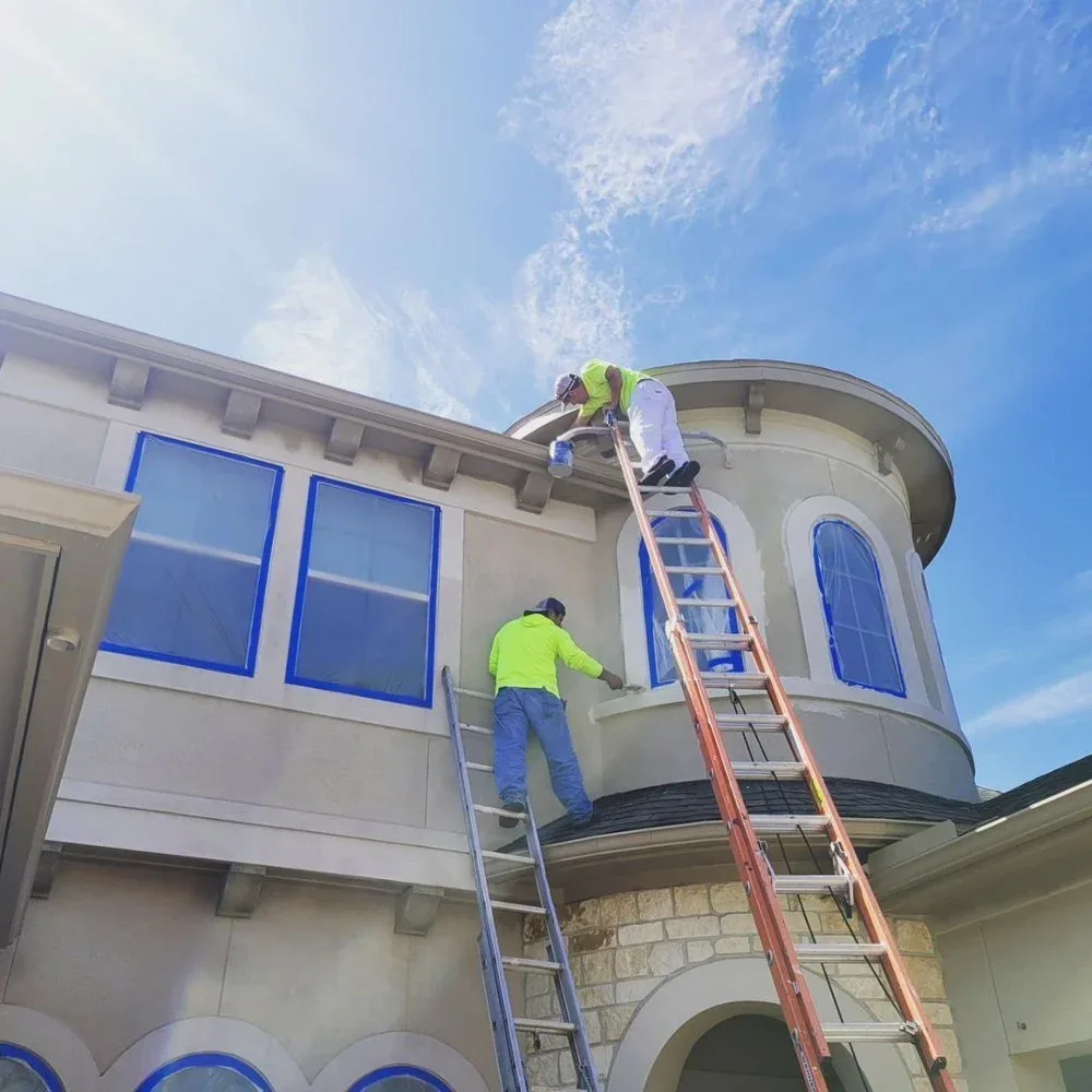 Professional painters working on a stucco home exterior in Sugar Land, TX by The Proud Paintbrush
